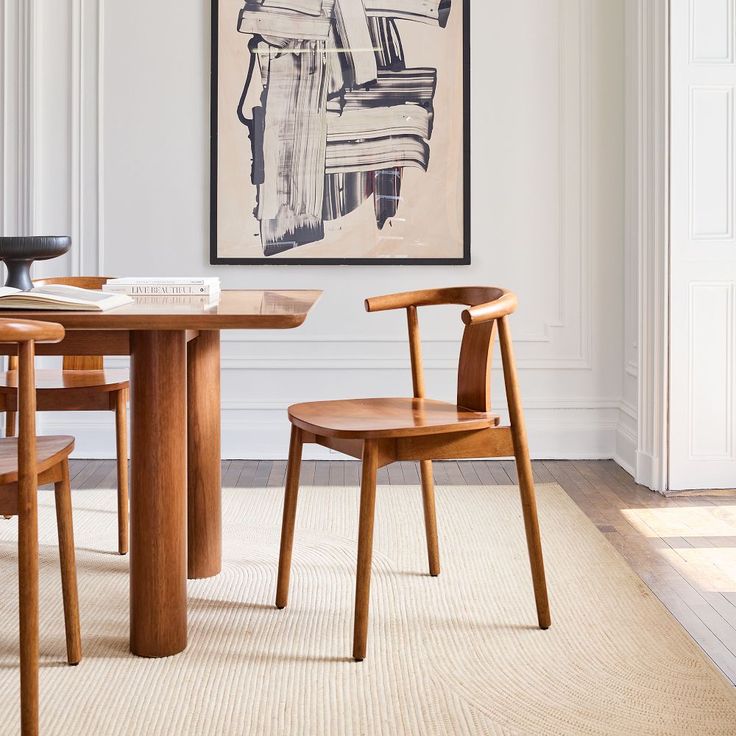 a dining room table with two chairs and a painting hanging on the wall above it