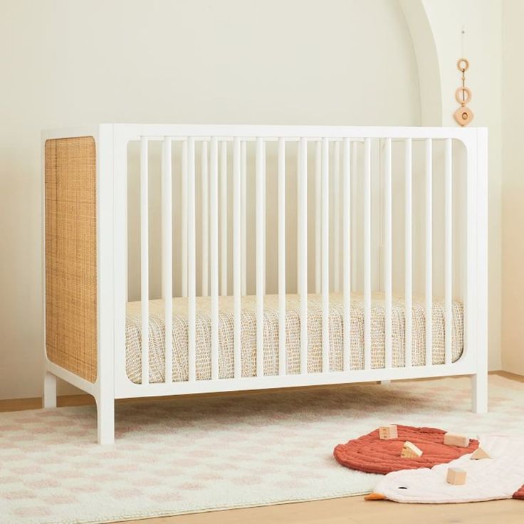 a white crib sitting on top of a wooden floor next to a rug and wall