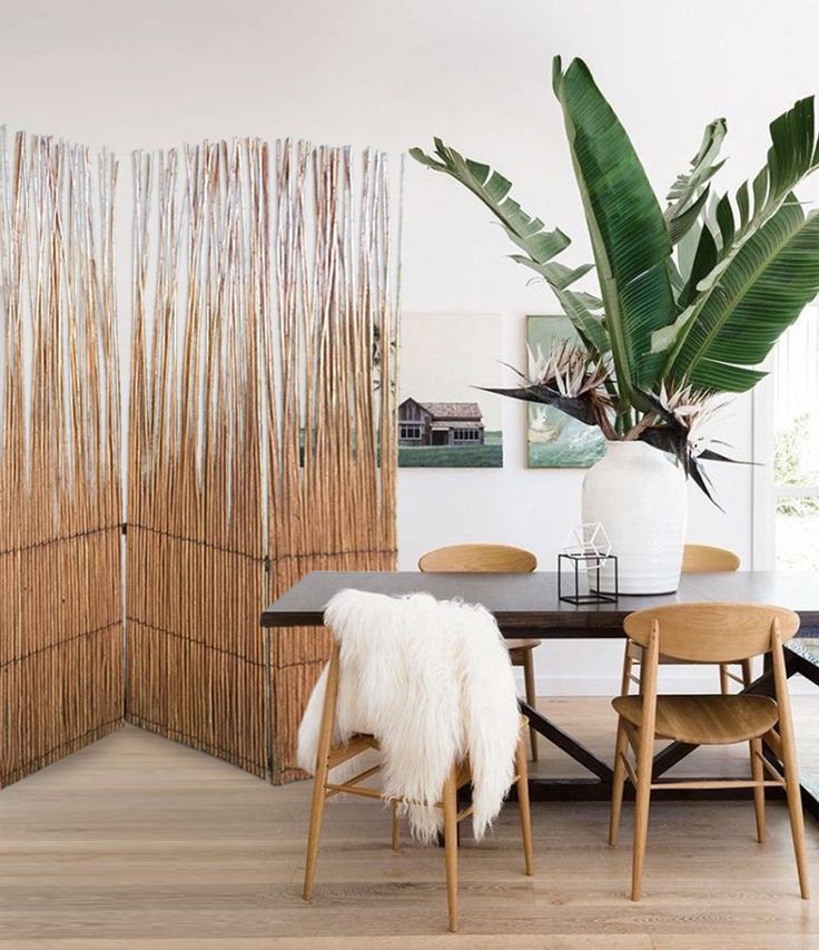 a room divider made out of bamboo sticks with chairs around it and a plant in the corner