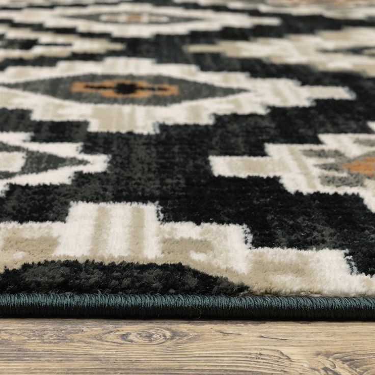 a black and white rug with an intricate design on the bottom corner, in front of a wooden floor