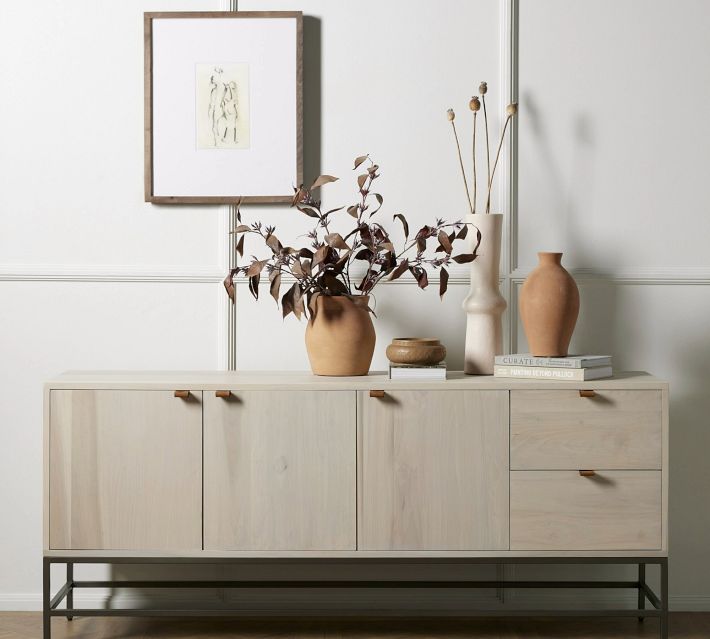 two vases on top of a wooden dresser next to a plant and pictures hanging on the wall