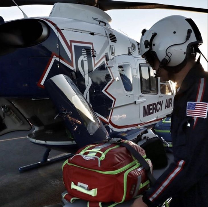 a man in uniform standing next to a helicopter with an american flag backpack on it