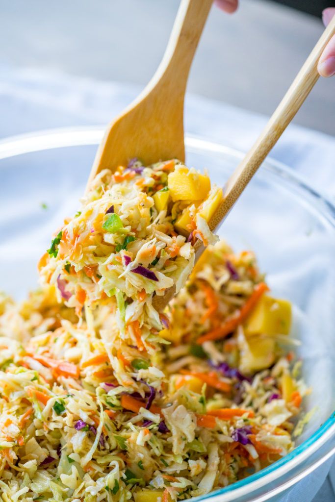 a person is scooping coleslaw out of a bowl with a wooden spoon