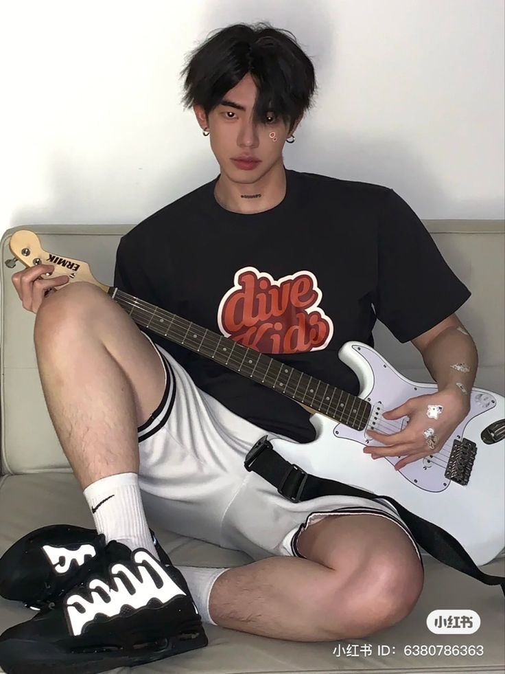 a man sitting on top of a couch with a guitar in his hand and wearing black shoes