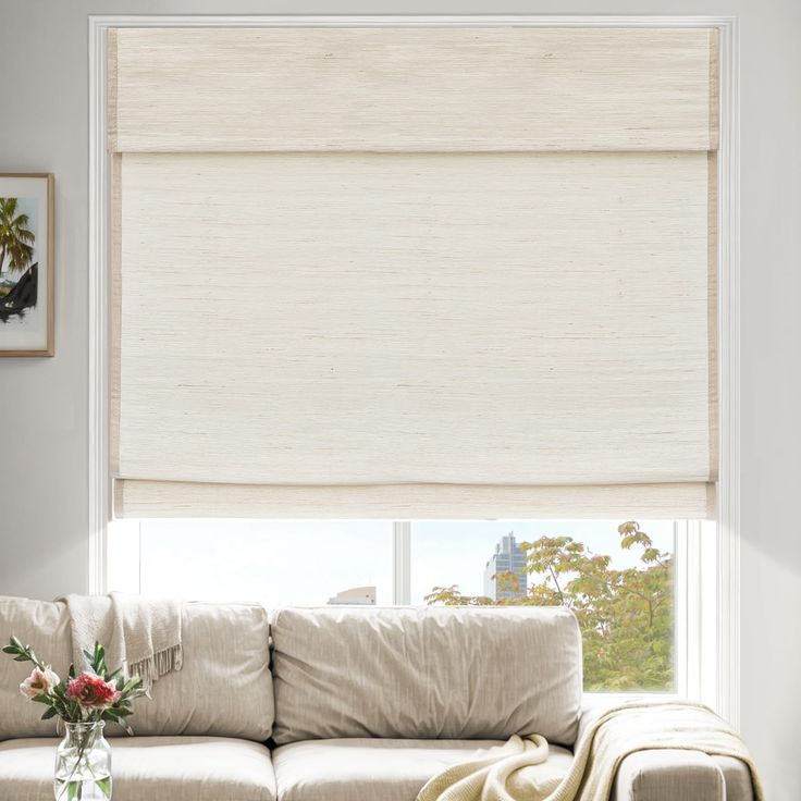 a living room with a white couch and large window covered in roman blind shades on the windowsill