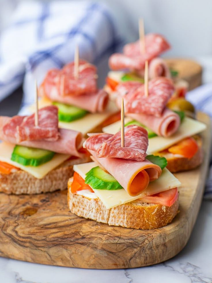 small sandwiches with meats and cheese are on a cutting board, ready to be served