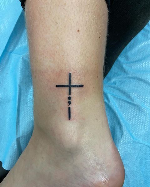 a cross tattoo on the foot of a woman's left leg is shown in black ink