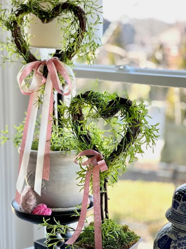 two potted plants are sitting on a table near a window with a heart shaped planter