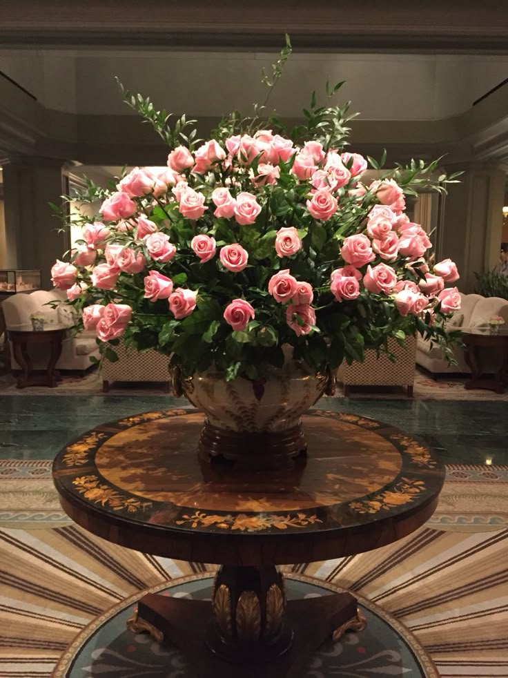 a vase filled with pink flowers sitting on top of a wooden table next to a mirror