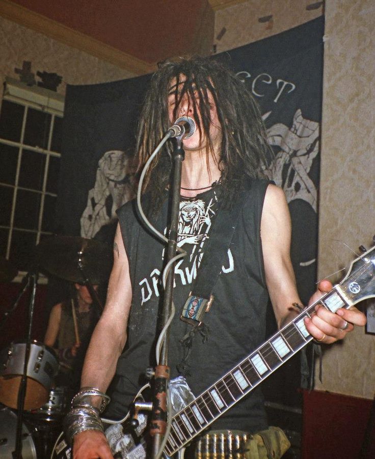 a man with dreadlocks on his face playing guitar in front of a microphone