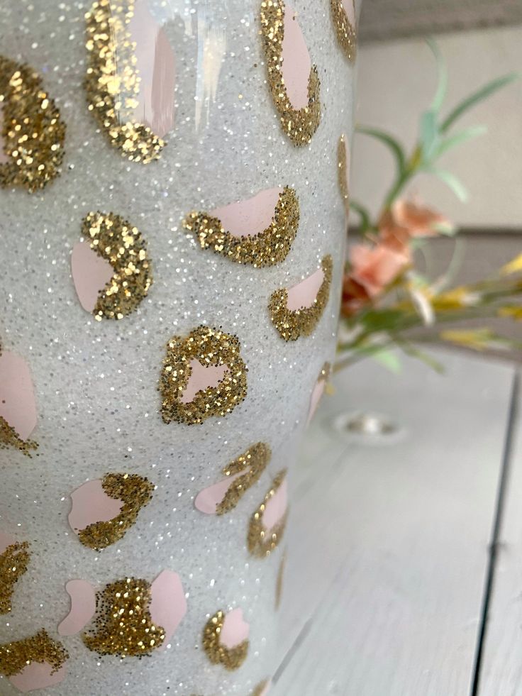 a white vase with gold and pink designs on the side sitting on a wooden table