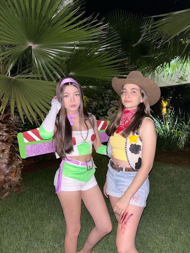 two women dressed in costumes standing next to each other on the grass with palm trees behind them