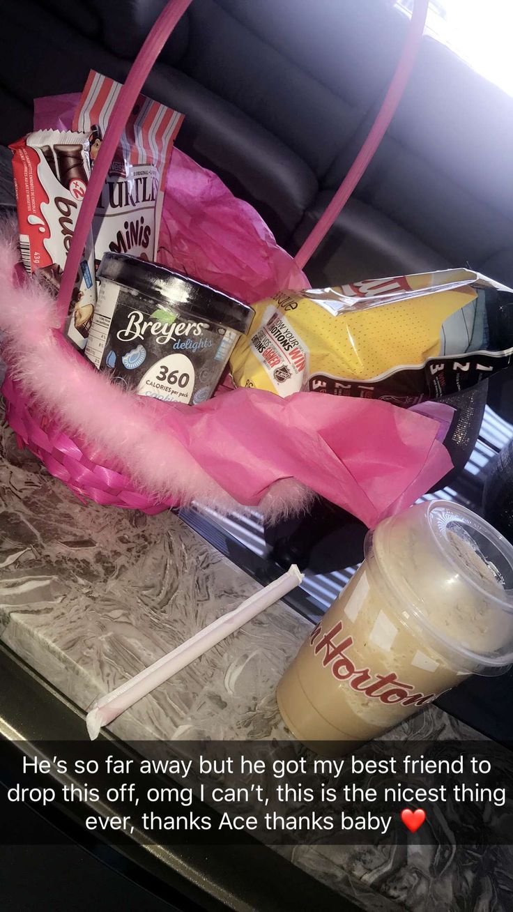 a pink basket filled with drinks and snacks on top of a table next to a cup