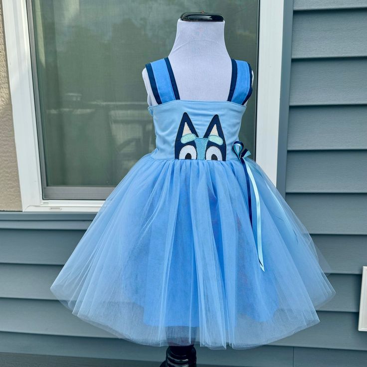 Blue dog character dress with a tulle overlay skirt and a double ribbon bow on the side. This dress features a sweet character dog embroidery design with her peeking up from the bodice.  The shoulder straps allow for ease of dressing, and the back of the bodice has encased elastic that will stretch allowing for longer wear. This dress can be layered with a shirt underneath for cooler weather or wear as a sundress for warmer days. Would be a cute dress to wear at a themed birthday party or even as a flower girl at a wedding.  All of my dresses and outfits are hand made by myself one at a time in my small studio. I try to source American made supplies whenever available.  Sizes are from 9-12 months to 5T. This item ships within 2 weeks. I do have a few sizes pre-made so they will ship the ne Dog Party Dress, Tulle Overlay Skirt, Ariel Hair, Toddler Projects, Dog Embroidery Designs, Toddler Party Dress, Sisters Dress, Kids Party Dresses, Blue Party Dress