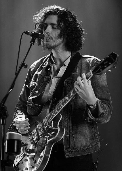 a man with long hair playing an electric guitar in front of a microphone on stage