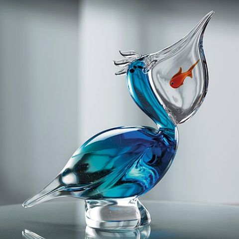 a glass bird figurine with a goldfish in it's beak sitting on a table