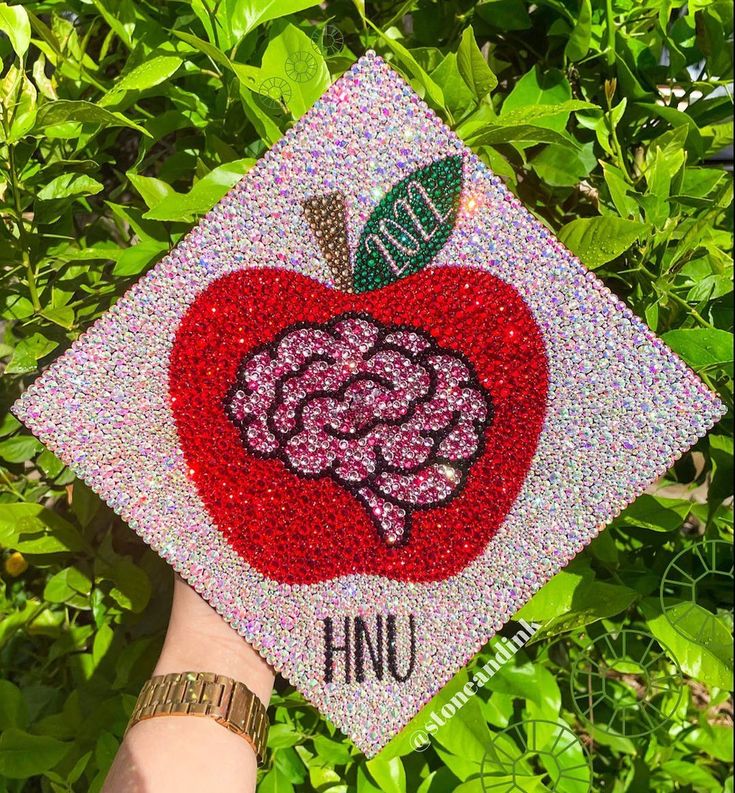 someone is holding up a graduation cap with an apple on it in front of some bushes