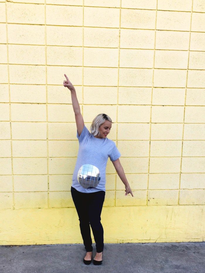 a pregnant woman standing in front of a yellow brick wall with her arms raised up