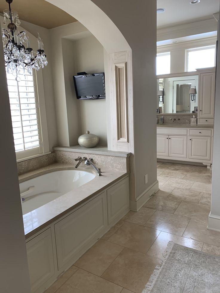 a large bath tub sitting under a window next to a tv mounted on a wall