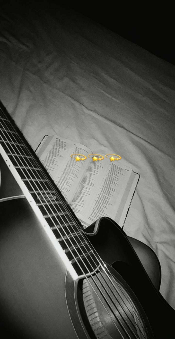 an acoustic guitar laying on top of a bed next to an open book and pen