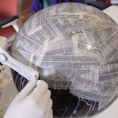 a person in white gloves is working on a large paper ball with newspaper pages all over it