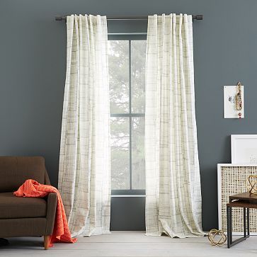 a living room filled with furniture and a window covered in white drapes next to a brown chair