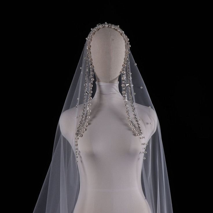 a white wedding veil with crystal beading on the top and bottom, in front of a mannequin's torso