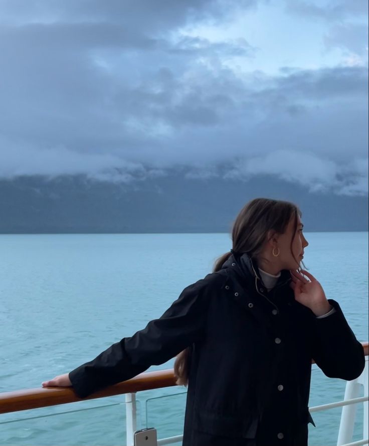 a woman standing on the deck of a boat looking out at the water and mountains