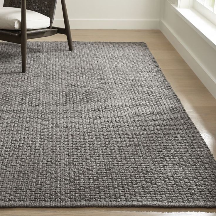 a gray rug in the corner of a room with a chair and window behind it