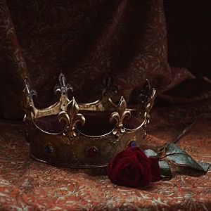 a crown and a rose on a bed with a brown cloth behind it that is covered in red fabric