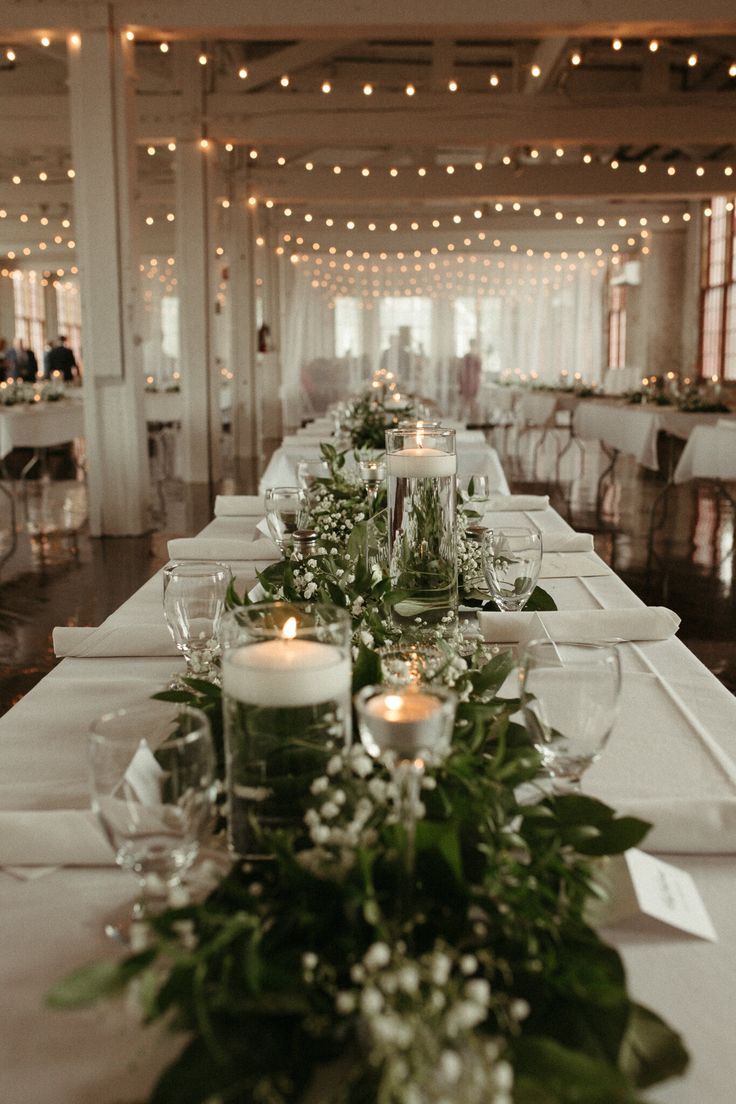 a long table with candles and greenery on it in a room filled with tables