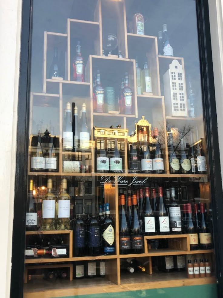 bottles of wine are displayed behind glass in front of a storefront window with shelves