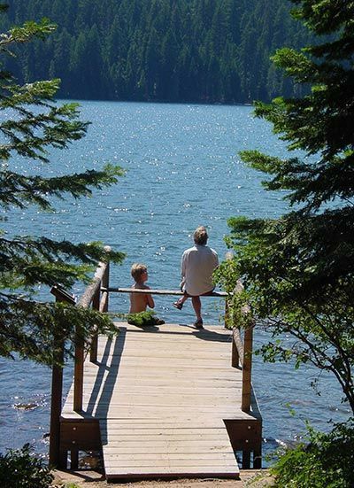 an older man and young child are sitting on a dock by the water looking out to the woods