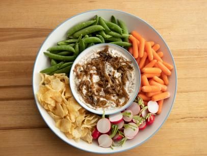 a white plate topped with veggies and dip next to chips on a wooden table