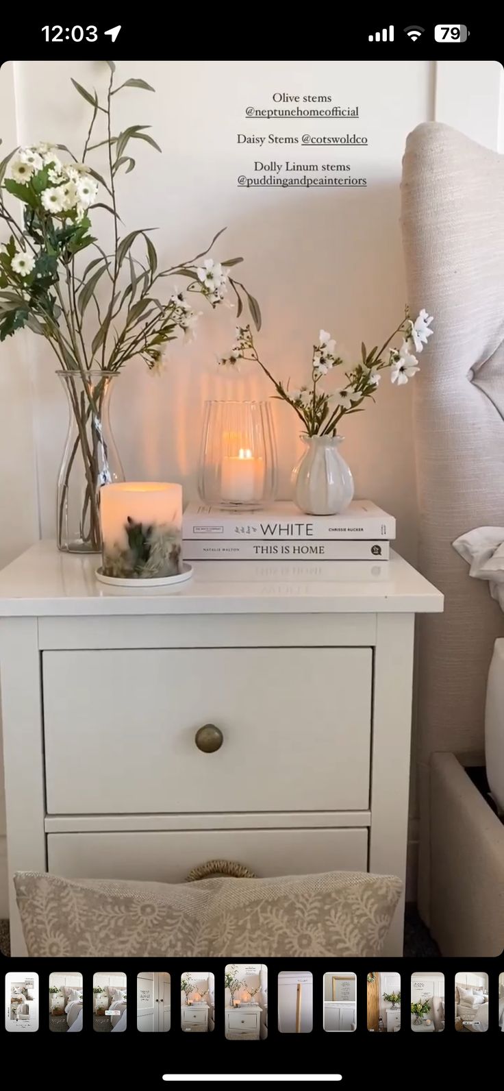 a white nightstand with flowers and candles on it in front of a bed side table