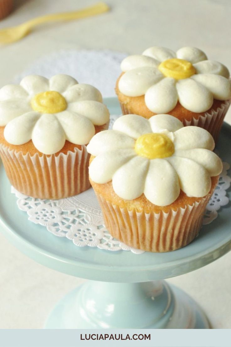 three cupcakes with white frosting and yellow centers on a blue cake plate