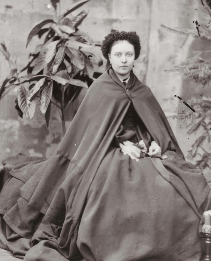 an old black and white photo of a woman in a dress with a cape on