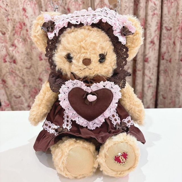 a brown teddy bear wearing a dress and holding a heart shaped keychain on top of a table