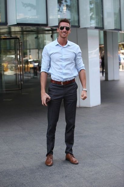 a man standing in front of a building wearing sunglasses and a blue shirt with brown pants