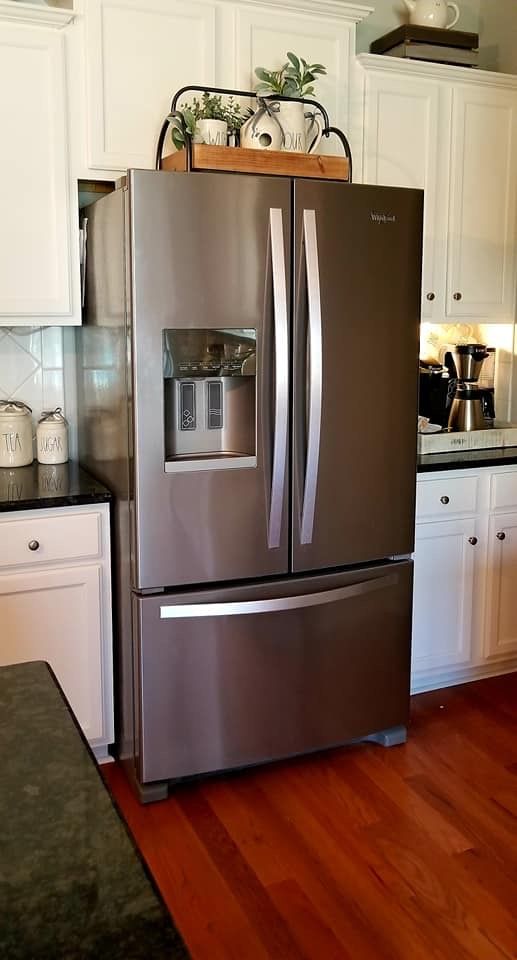 a metallic refrigerator freezer sitting inside of a kitchen next to white cabinets and wooden floors