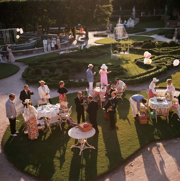 a group of people standing around a lush green field next to a formal dinner table