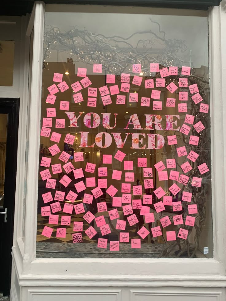 a store window with pink sticky notes attached to the glass and writing you are loved