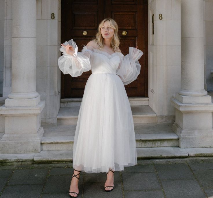 a woman standing in front of a door wearing a white dress and holding an object