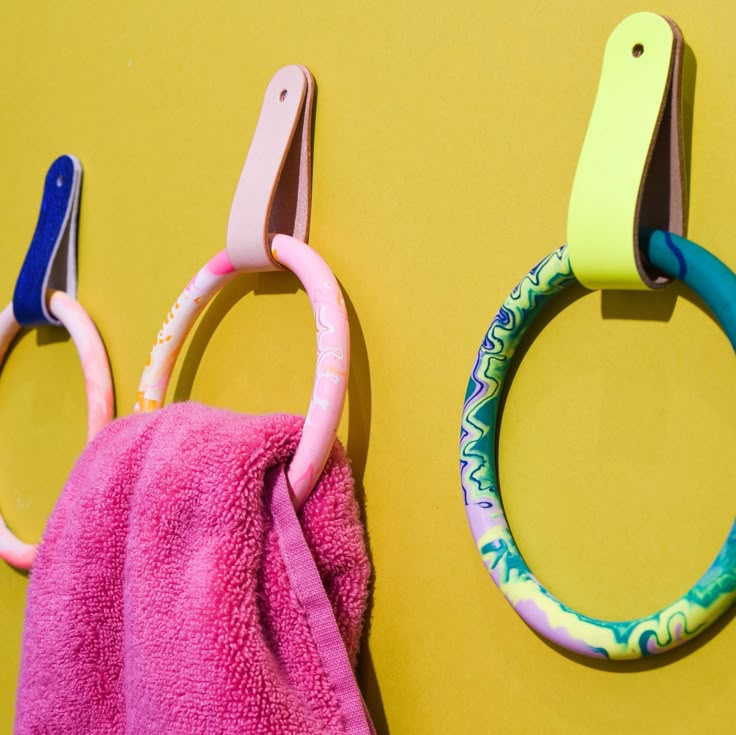 two pairs of scissors hanging from hooks on a yellow wall next to a pink towel