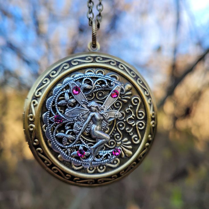 "Beautiful large fairy locket necklace for those who love fantasy jewelry.  Let this playful little sterling silver plated fairy guard over your most precious memories while perched atop a crescent moon.   This piece features fuchsia Swarovski rhinestones and a large antique brass Victorian styled locket.  The locket measures 46mm (approximately 2\") in diameter and it comes with a chain in the length of your choice. Tip: If you are unsure what necklace length you need, then you should use a pie Fantasy Engraved Jewelry For Fantasy Events, Fantasy Brass Jewelry For Gifts, Whimsical Metal Jewelry With Vintage Charm, Whimsical Vintage Charm Jewelry, Magical Metal Necklaces For Gifts, Whimsical Vintage Charm Pendant Jewelry, Magical Charms For Jewelry Making, Magical Silver Charm Necklaces As Gift, Handmade Silver Fairycore Jewelry