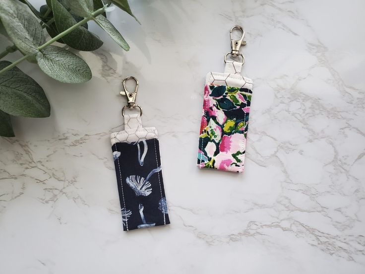 two key chains with flowers on them sitting next to a plant