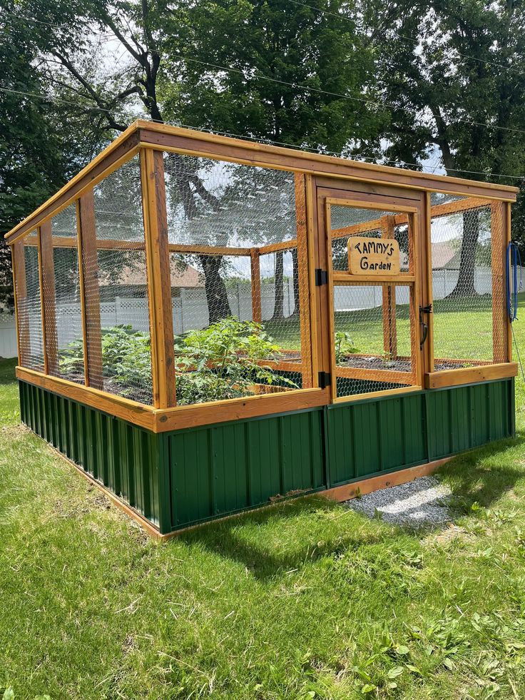 a small green house sitting in the middle of a grass covered field with plants growing inside