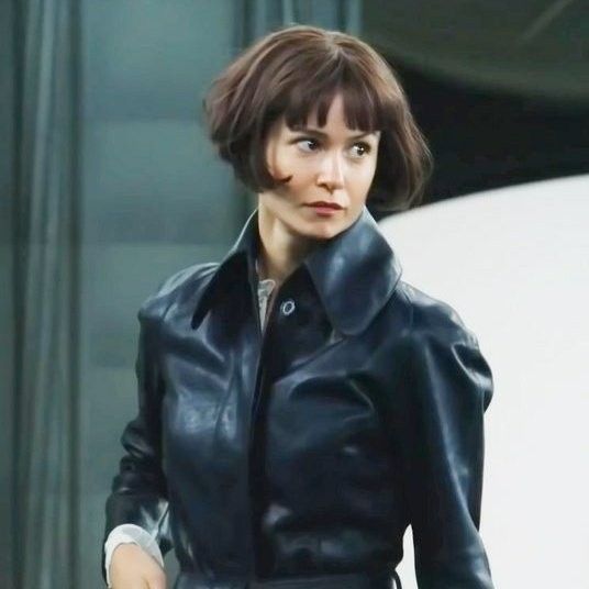 a woman in a black leather jacket is walking down the street with her hand on her hip