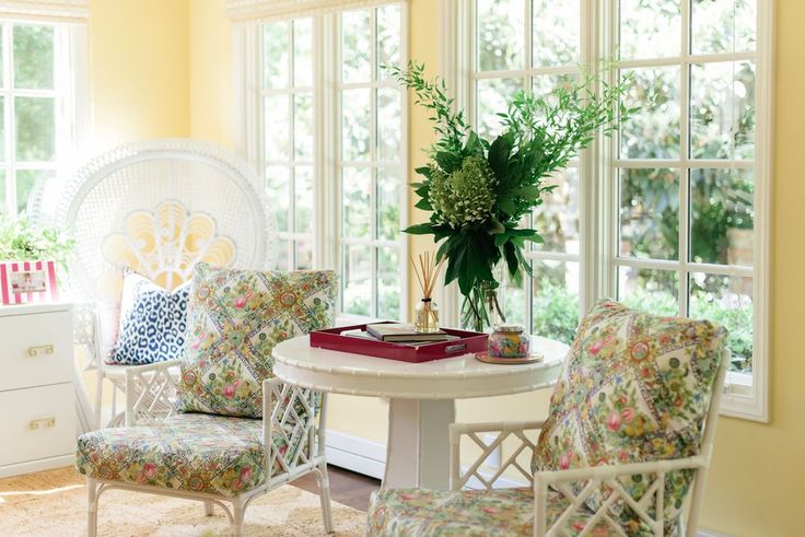 a white table with chairs and a book on it in front of two large windows