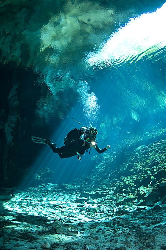 a person scubas in an underwater cave with sunlight streaming through the water's walls